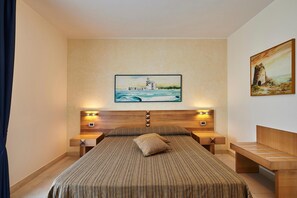 A hotel room with a bed, two bedside tables, a headboard, and artwork on the walls.