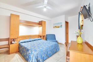 A hotel room with a bed, a chair, a desk, a television, and a painting on the wall.