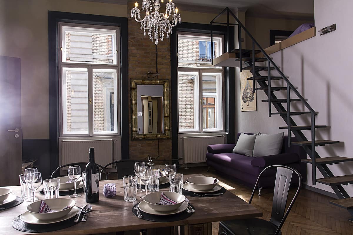 A dining area with a table set for four, a chandelier, and a staircase leading to an upper level.