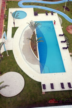 Une piscine rectangulaire à bords incurvés, entourée d’une terrasse blanche et de palmiers.