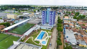 Vista aérea de una zona residencial con un amplio campo deportivo, piscina y dos edificios azules destacados.