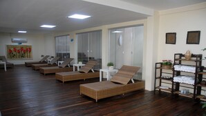 Una habitación con varias sillas reclinables de mimbre, una mesita y un estante con toallas y adornos.
