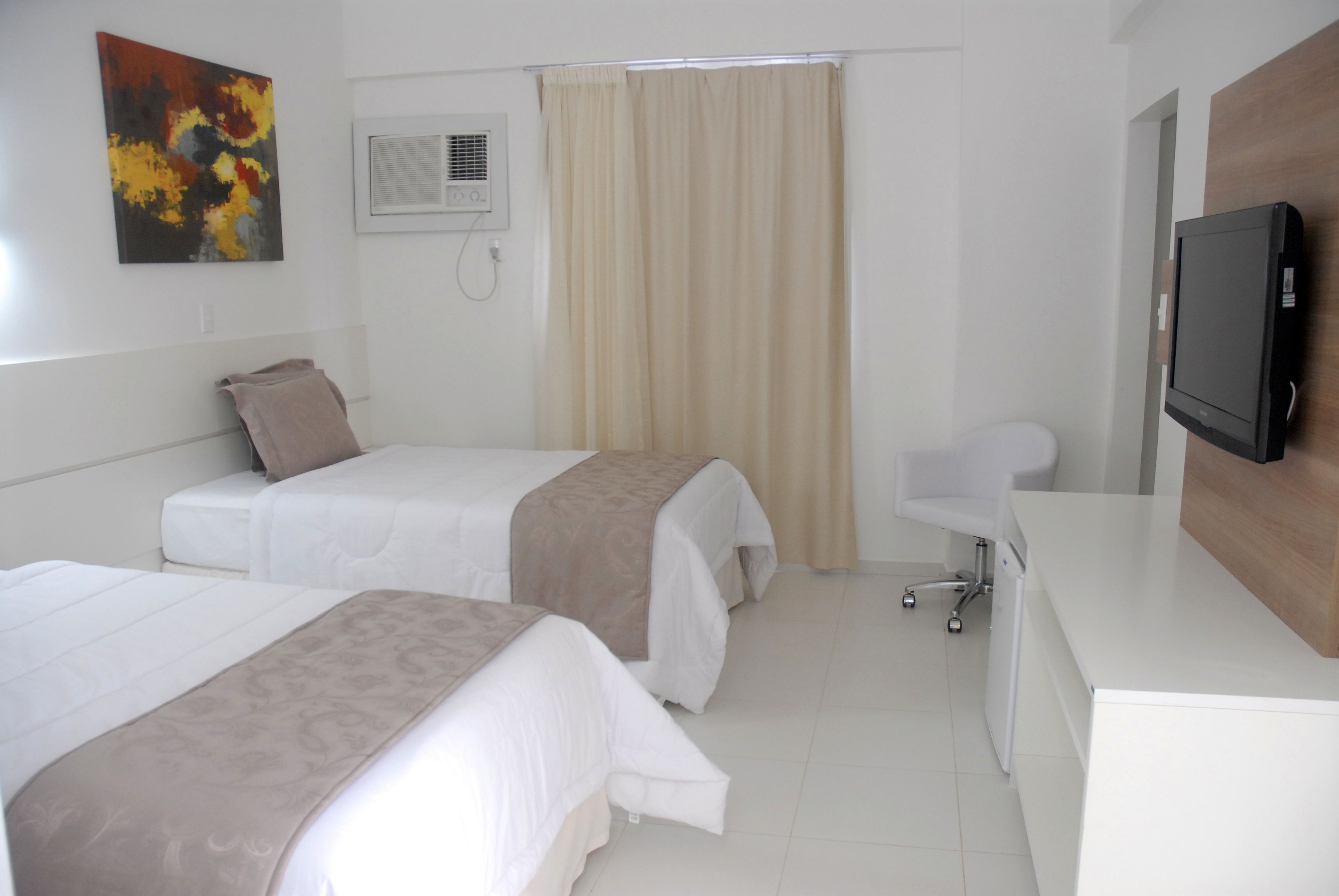 Habitación de hotel con dos camas, un escritorio, televisión y ventana con cortinas.