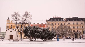 Ein Hotel mit roter und weißer Fassade, einem Glockenturm und einem verschneiten Innenhof mit Bänken und Bäumen.