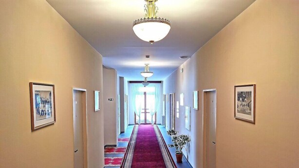 Ein Hotel-Flur mit rotem Teppich, gerahmten Bildern an den Wänden und einem Kronleuchter.