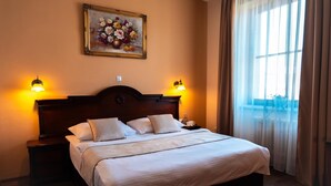 Ein Hotelzimmer mit einem großen Bett, zwei Nachttischlampen, einem Bild an der Wand und einem Fenster mit Vorhängen.