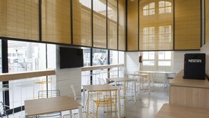 Un caffè moderno con soffitti alti, ampie finestre e diversi posti a sedere, tra cui tavoli e sedie.