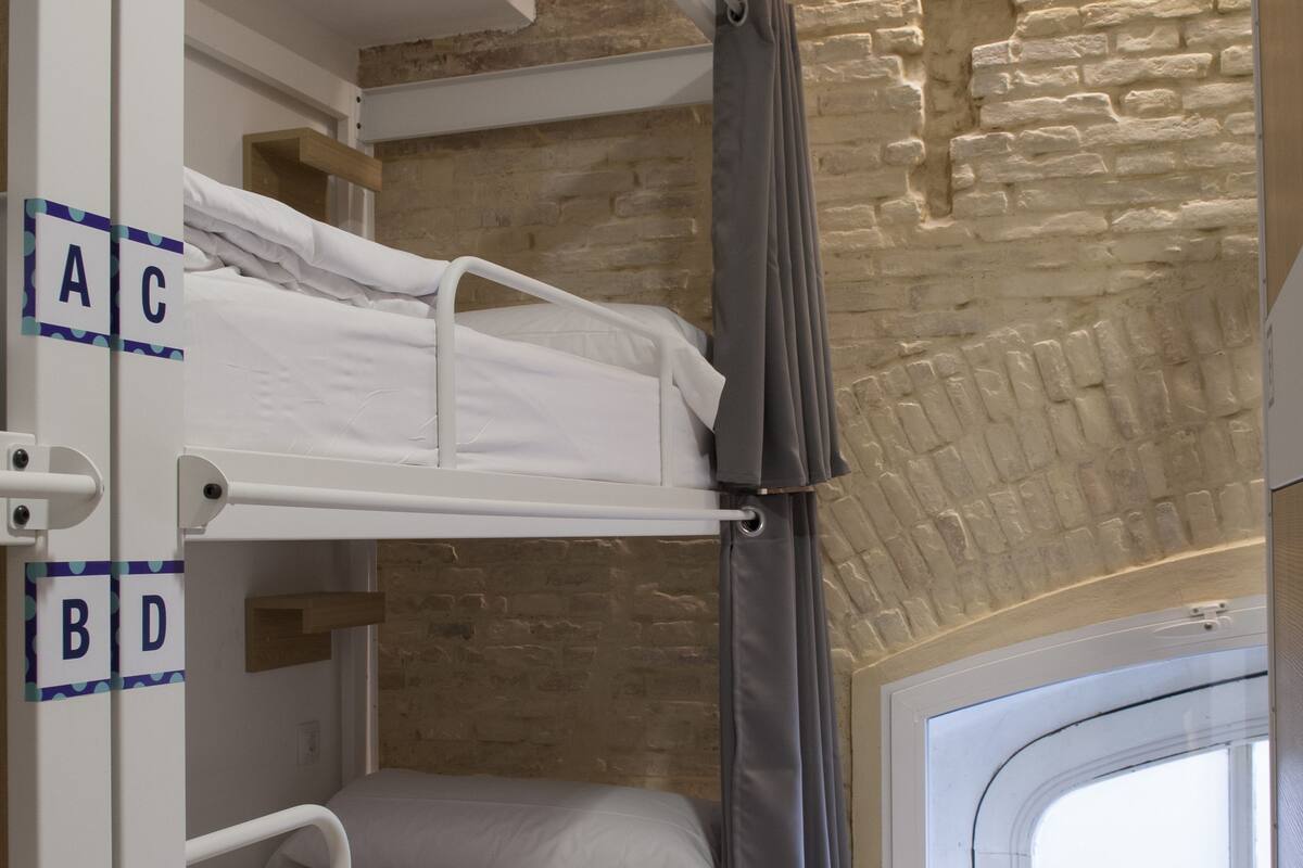 A bunk bed room with a stone wall and a window.