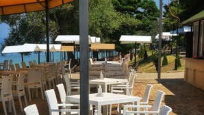 Espace extérieur aménagé avec des tables et des chaises blanches, des parasols et une zone dallée.