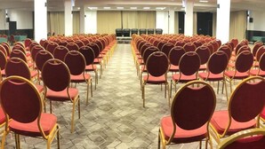 Une salle de conférence avec des rangées de chaises rouges et un sol orné d’un motif hexagonal.