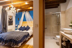 Quarto com cama, mesa de cabeceira, lustre e banheiro com chuveiro e vaso sanitário.