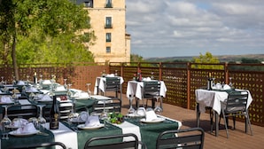 An outdoor dining area with tables set for a meal, a view of a castle in the background, and a wooden deck. - Posada De Eufrasio (Lerma)