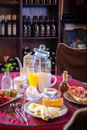Uma mesa de café da manhã com diversos alimentos, um bule, um jarro e uma garrafa de azeite.