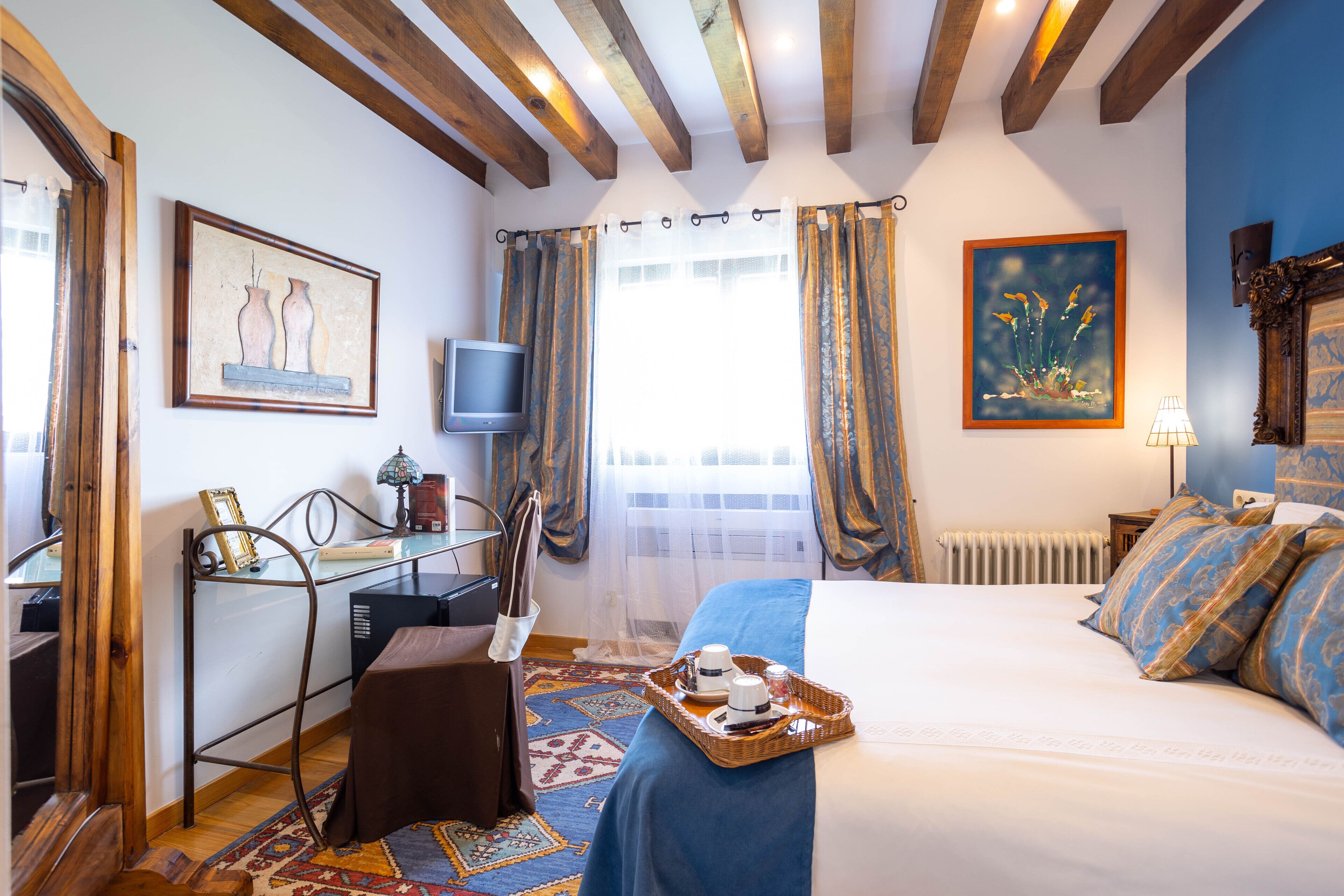 Une chambre d’hôtel avec un lit, un bureau avec une télévision, une fenêtre avec des rideaux et des œuvres d’art accrochées aux murs.