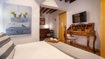 A bedroom with a bed, a wooden desk, a television, and a painting of suitcases with flowers.