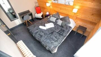 A modern hotel room with a large bed, a desk, a chair, and a suitcase.