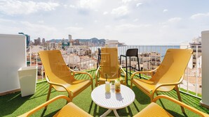 A terrace with yellow chairs and a table, overlooking a cityscape with buildings and a body of water. - Hotel Queens (Benidorm)