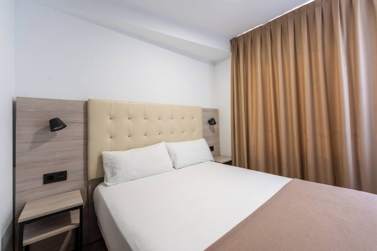 A neatly made bed with white linens, a headboard with a tufted design, and a bedside table with a lamp.