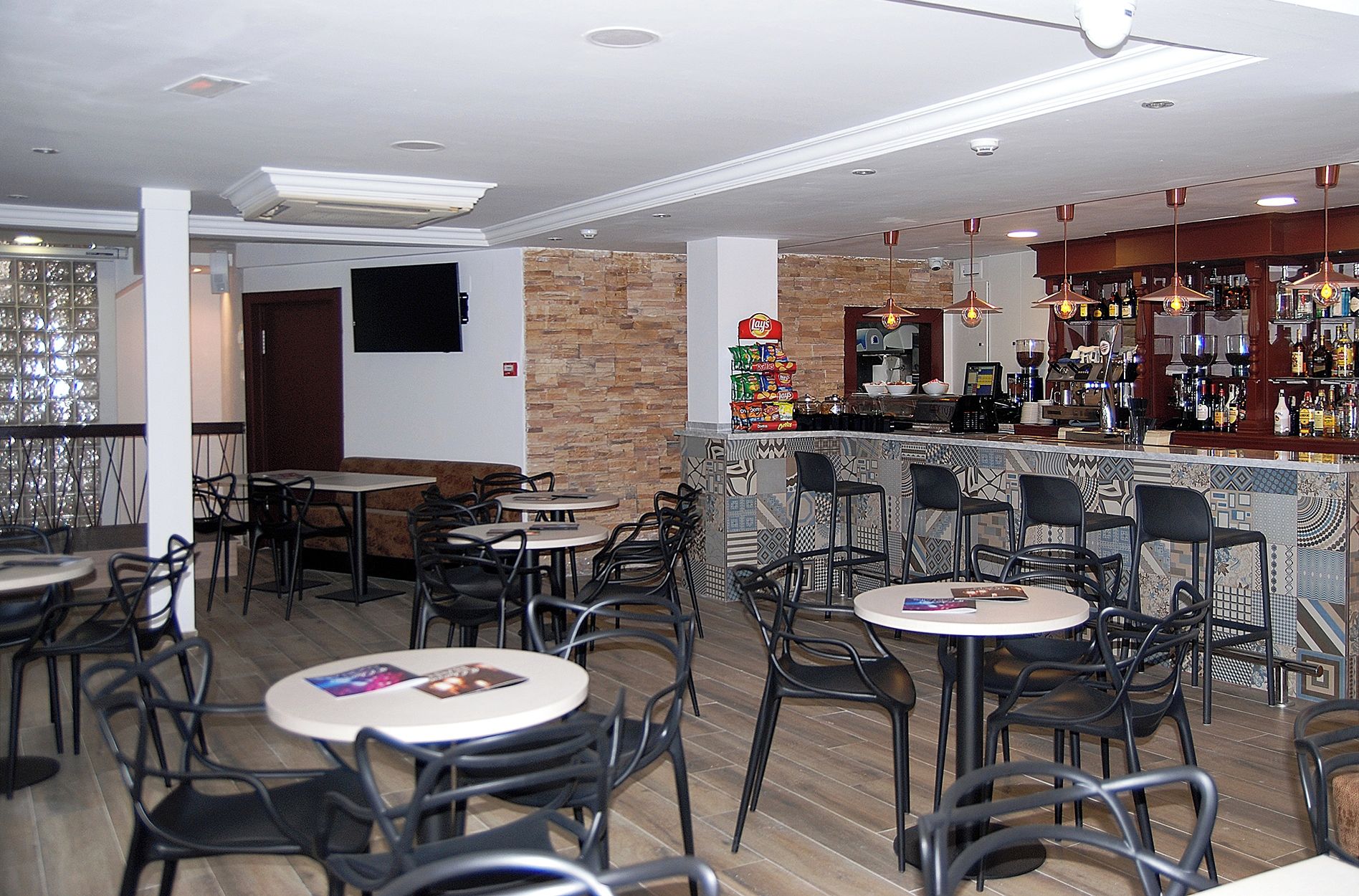 Ein Restaurant mit mehreren Tischen und Stühlen, einer Bar mit einer Auswahl an Flaschen sowie einer Wand aus Stein.