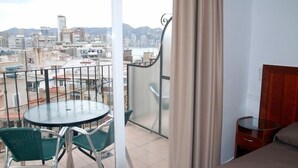 A balcony with a table and chairs, a view of a cityscape, and a bed with a wooden headboard. - Hotel Queens (Benidorm)