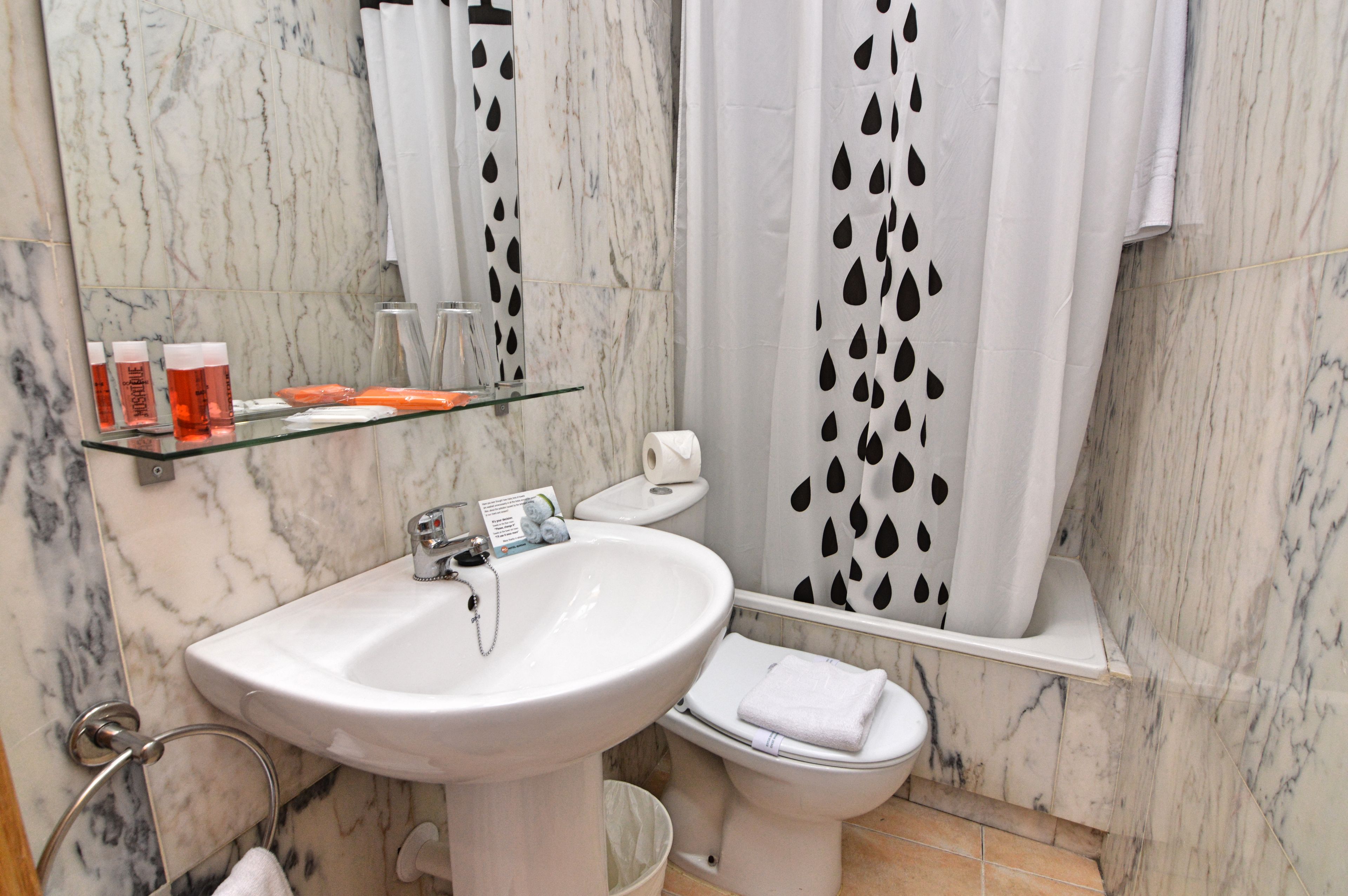 Ein Badezimmer mit Marmorwaschtisch, Toilette und Duschvorhang mit Blätermuster.