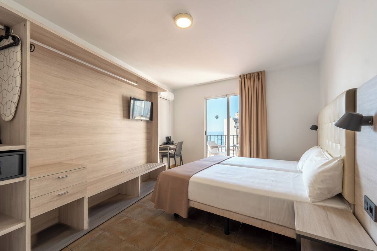 A hotel room with a bed, a desk, a chair, a TV, and a balcony with a view.