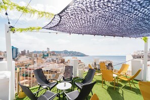A terrace with outdoor seating, a view of the city, and a beach in the distance. - Hotel Queens (Benidorm)