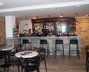 A bar area with a counter, bar stools, and a variety of bottles. - Hotel Queens (Benidorm)