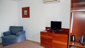 A room with a bed, a blue armchair, a wooden dresser with a flat-screen TV, and a wooden wardrobe. - Hotel Queens (Benidorm)
