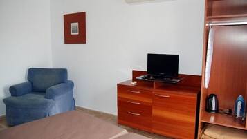 Een kamer met een bed, een blauwe fauteuil, een houten dressoir en een houten kledingkast.
