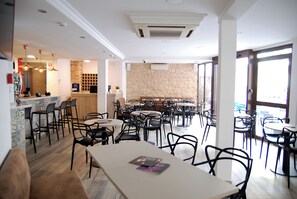 A restaurant with multiple tables and chairs, a bar area, and a stone wall.