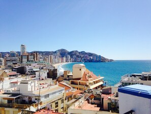A coastal cityscape with a mix of residential and commercial buildings, a clear blue sky, and a beach in the distance.