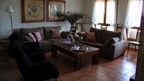 Sala de estar con dos sofás, una mesa de centro y una lámpara de pie. Hay cuadros enmarcados en la pared y una ventana con cortinas.
