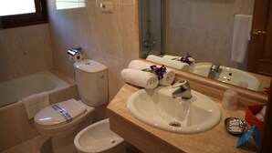 Un baño con inodoro, bidé, lavamanos y un espejo grande.