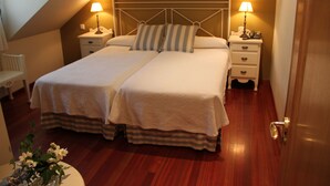 Una cama doble con un cojín a rayas, dos mesitas de noche con lámparas y suelo de madera.