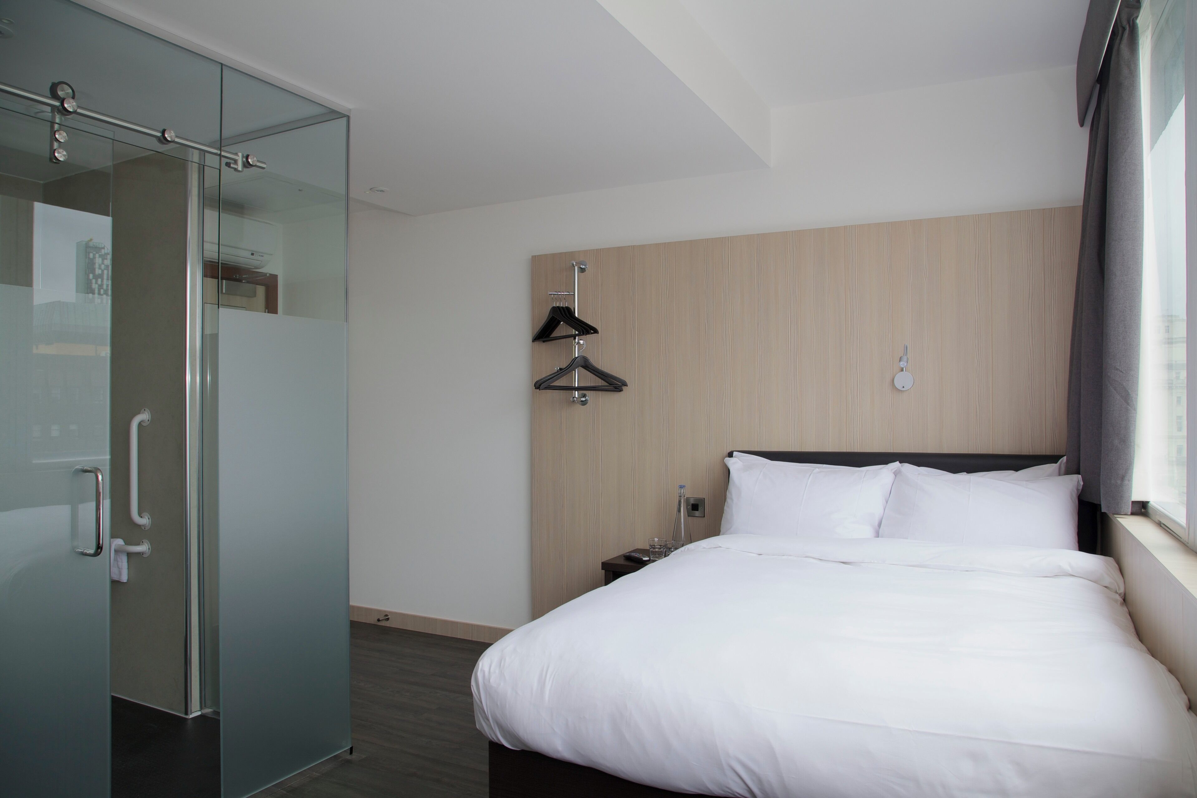 Ein Hotelzimmer mit Bett, Schrank, Nachttisch und einem Fenster mit Vorhängen.