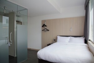 Una habitación de hotel con cama, armario, mesita de noche y ventana con cortinas.