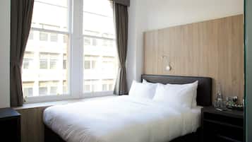 A hotel room with a large bed, a wooden headboard, a nightstand, and a window with curtains.