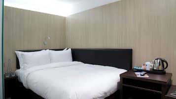 Habitación de hotel con una cama bien hecha, una mesita de noche con cafetera y una lámpara.