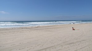 A wide sandy beach with footprints and a person lying on the sand.