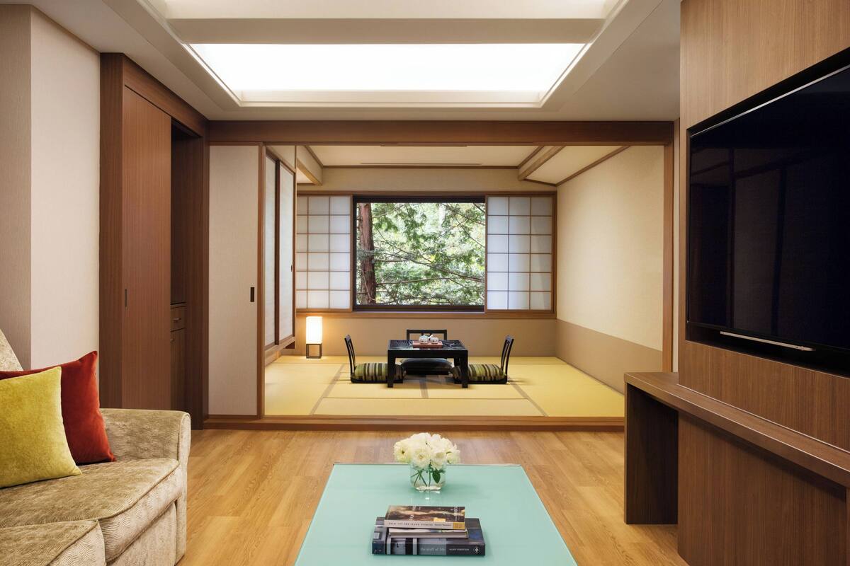 A traditional Japanese room with tatami flooring, a tatami mat table, a sofa, a TV, and a bookshelf.