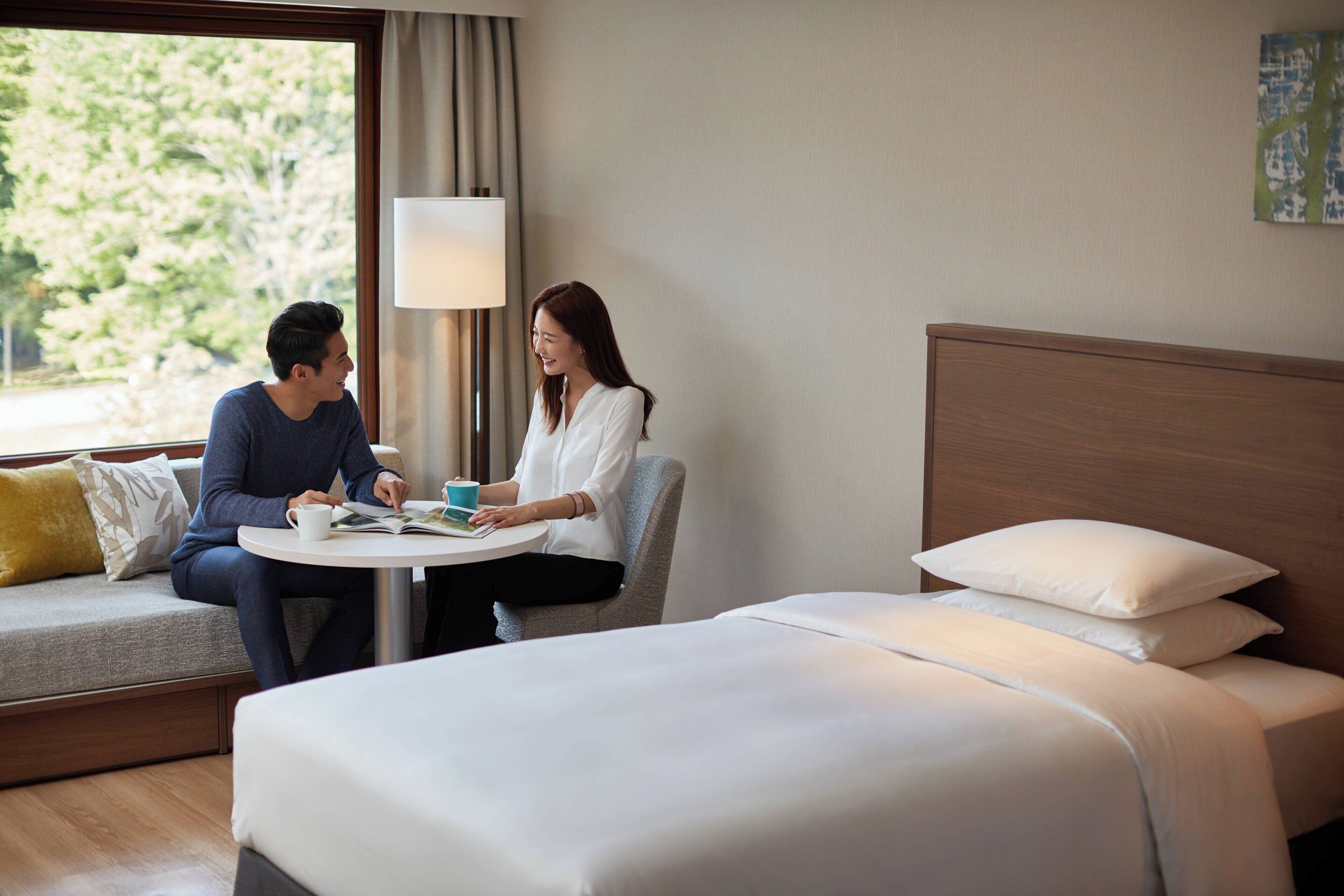 A hotel room with a bed, a sofa, a table, and a lamp.