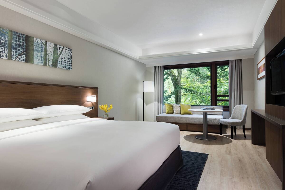 A modern hotel room with a large bed, a seating area with a table, and a TV.