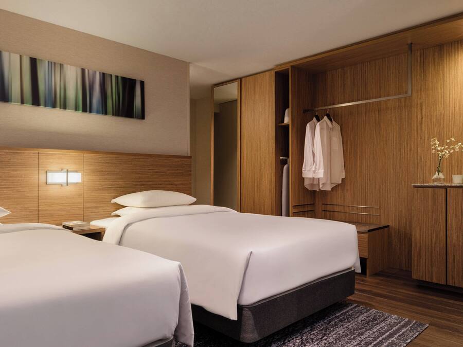 A hotel room with two beds, a wooden wardrobe, a painting on the wall, and a small table with a vase of flowers.