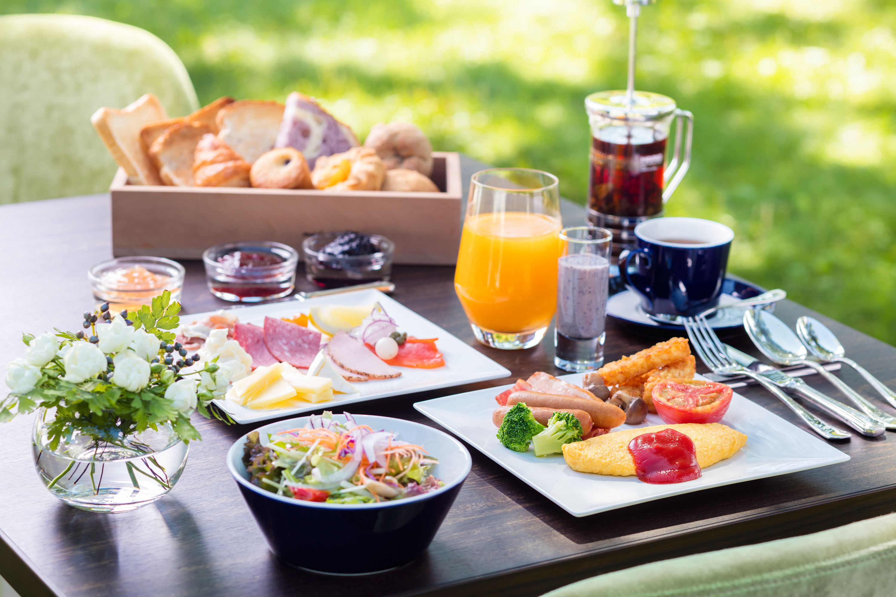 A breakfast table with various food items, a pitcher of juice, and a vase of flowers.