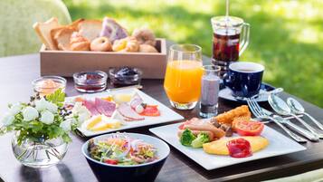 A breakfast table with various food items, a pitcher of juice, and a vase of flowers.