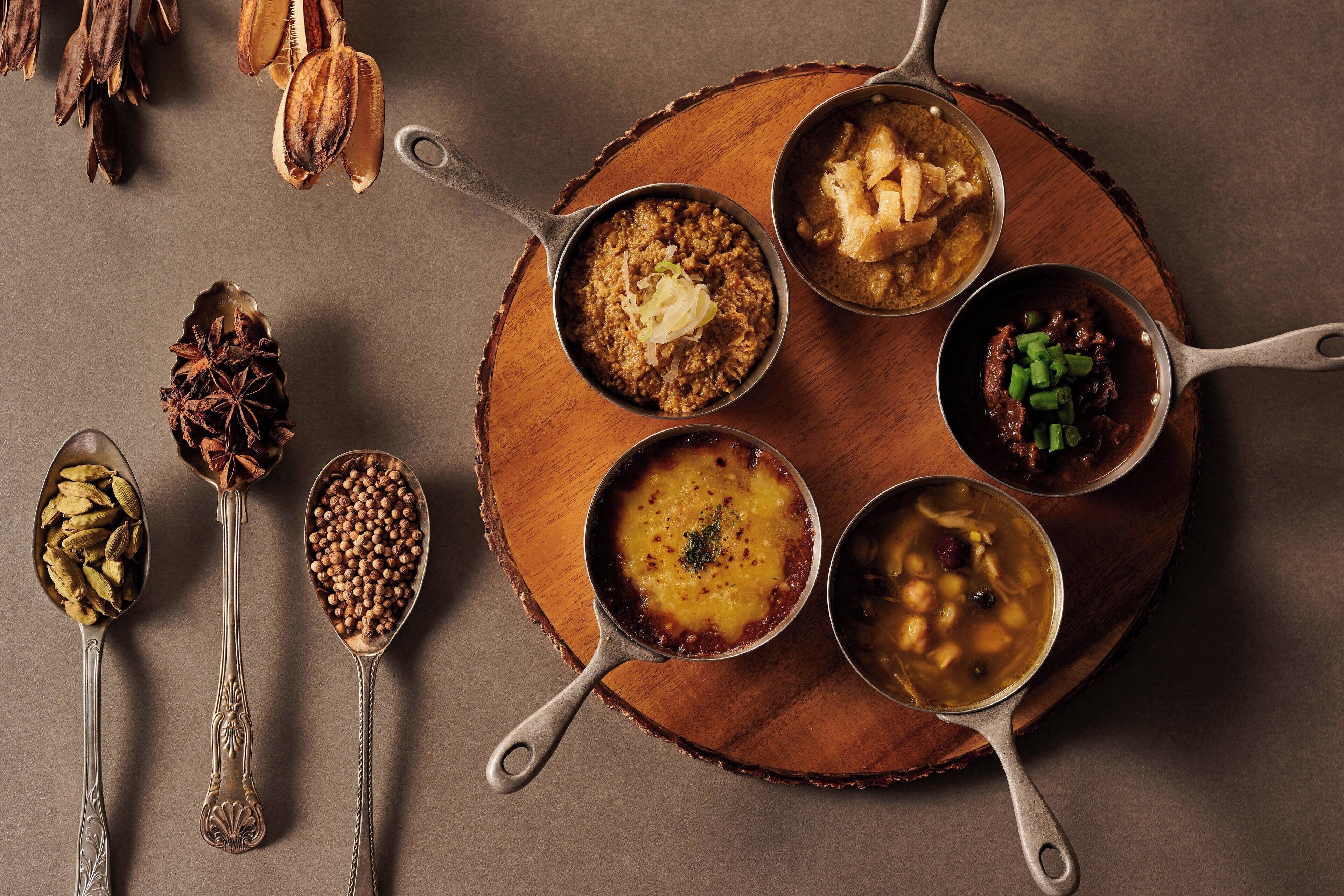 A wooden table with five metal pans containing different dishes.
