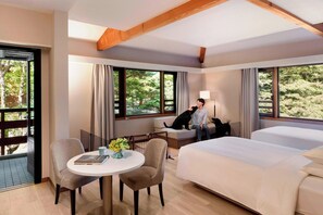Une chambre d’hôtel dotée d’un grand lit, d’un coin salon avec une table et des chaises, et de grandes fenêtres donnant sur un paysage verdoyant.