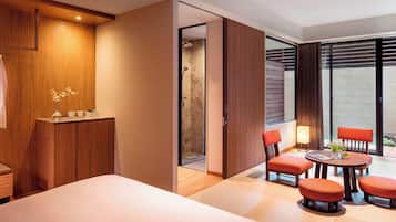 Ein modernes Hotelzimmer mit einem großen Bett, einem Holzschrank, einer Sitzecke mit orangefarbenen Sesseln und einem großen Fenster mit Blick.