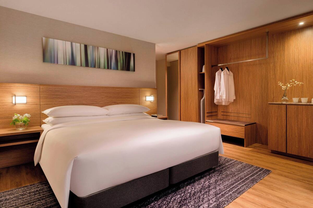 A modern hotel room with a large bed, wooden wardrobe, and a painting on the wall.